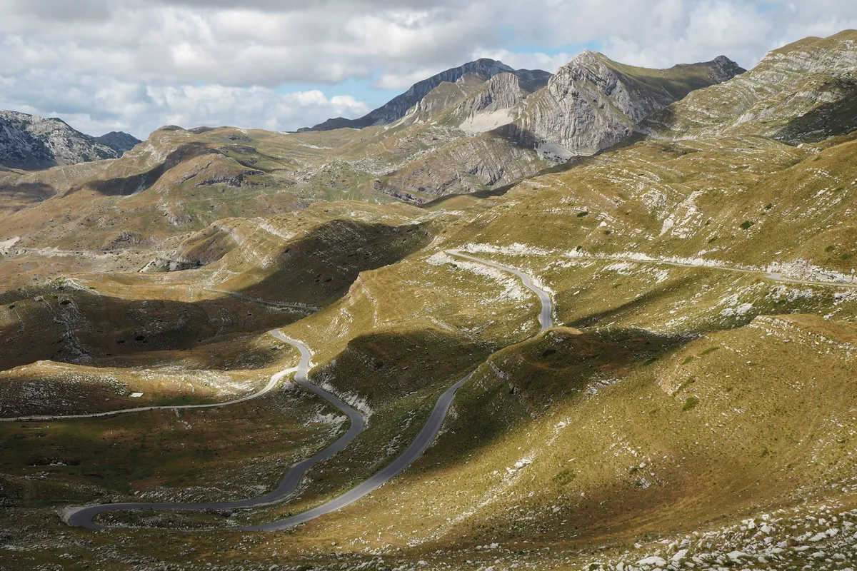 Een kronkelende weg over een hoge karstvlakte, onder de bergtoppen